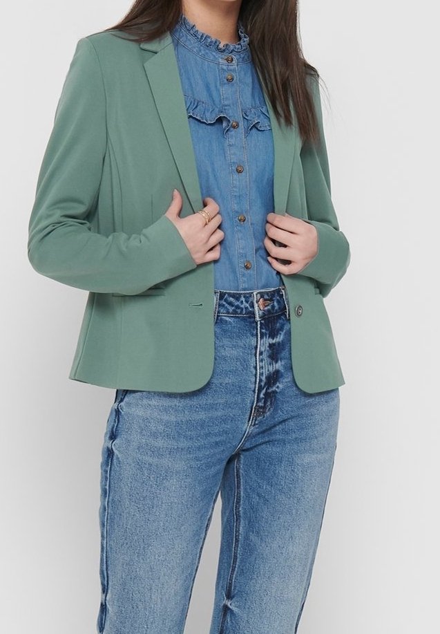 Grön skräddarsydd kavaj med slagkrage, lätt tyg och enkelknappsstängning, bärs över en ljus denimskjorta och högmidjade jeans.