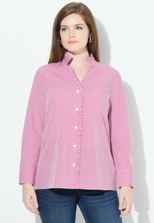 Camicia a righe rosse e bianche con colletto arricciato, maniche lunghe e bottoni bianchi. Indossata con jeans blu scuro.