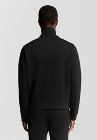 Zwarte zippered sweatshirt met hoge kraag, gemaakt van zachte stof, met een ontspannen pasvorm en eenvoudig ontwerp, gedragen met bijpassende broek.