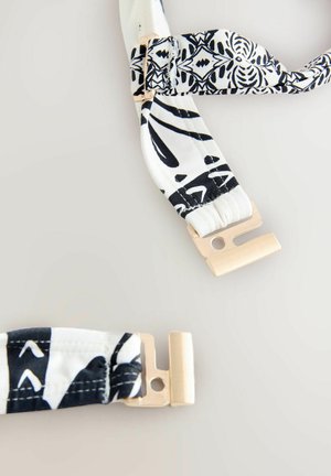 Mustavalkoinen kuvioitu kangasnauha, jossa kultaisten metallilukkojen päässä. Pehmeä rakenne; sisältää sekoituksen geometrisia ja orgaanisia kuvioita.