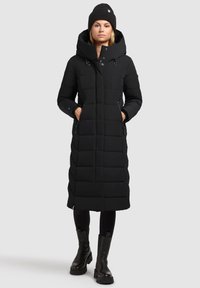 Black long puffer coat with a hood, featuring a quilted design, side pockets, and a straight fit, paired with black knee-high boots.