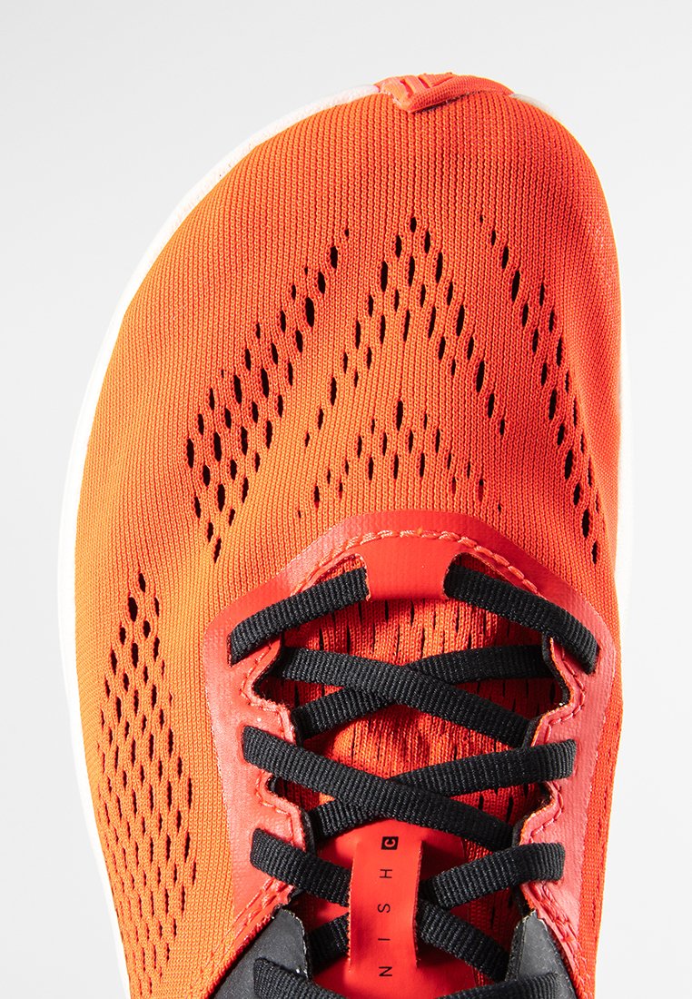 Zapatilla deportiva roja con parte superior de malla transpirable, cordones negros y suela de goma. Las perforaciones notables mejoran la ventilación.