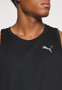 Czarny sportowy top na ramiączkach o prążkowanej fakturze, z małym szarym logo Puma na lewej części piersi. Klasyczny okrągły dekolt.