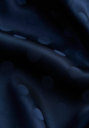 Tkanina námořnicky modrá s jemně vystouplými puntíky. Hladká textura s mírným leskem, který zvýrazňuje vzor puntíků na tmavém podkladu.