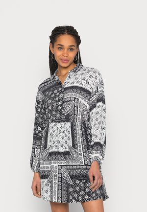 Vestido padrão preto e branco com mangas longas, colarinho e um ajuste relaxado, apresentando intrincados desenhos florais e geométricos.
