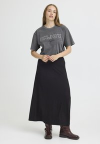 Sivá tričko s grafickým nápisom "UŽITE SI život" a krátkymi rukávmi, skombinované s čiernou dlhou sukňou. Hnedé členkové čižmy dotvárajú outfit.