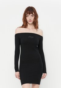 Svart avskåret kjole med lange ermer, tettsittende fasong og en jevn tekstur. Har rhinestonesdetaljer ved halsen.
