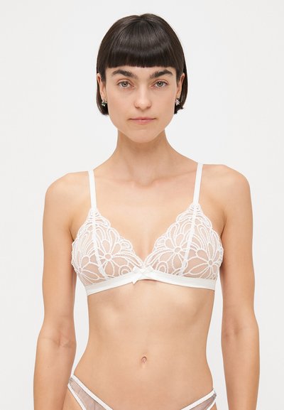 Bralette bianco in pizzo con motivo floreale, coppe triangolari, sottili spalline regolabili e un dettaglio a fiocco sul sottobanda liscia.