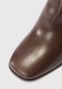 Acercamiento al área de los dedos de una bota de cuero marrón oscuro, lisa, con forma cuadrada y borde de suela negra.