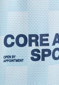 Tissu en maille sportive bleu avec le texte en gras "CORE A" et un texte plus petit "OUVERT SUR RENDEZ-VOUS" imprimés dessus.