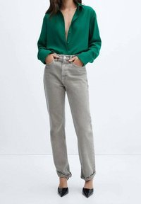 Chemise verte à boutons, à manches longues, associée à un jean taille haute gris clair. Tenue complétée par des escarpins noirs à bout pointu.