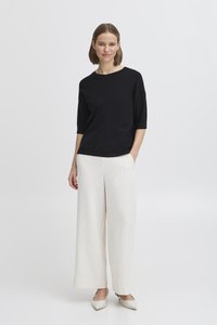 Czarny top z krótkim rękawem, białe szerokie, paskowane spodnie i białe buty na wskazujący czubek, wszystkie o gładkiej teksturze na jasnym tle.