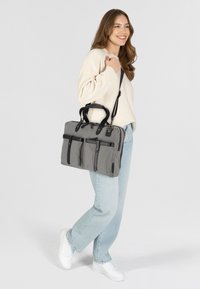 Bolsa para portátil de tela gris con acentos de cuero negro, múltiples bolsillos frontales, asas superiores y una correa de hombro desmontable.