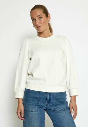 White sweatshirt with puffed sleeves, rounded neckline, and ribbed cuffs. Paired with blue high-waisted jeans, highlighting a casual style.