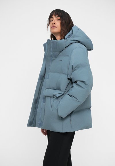 Svetlo modra puhovka z visokim ovratnikom in snemljivo kapuco. Ima sprednji zadrgo, stranske žepe in kvadratno teksturo.