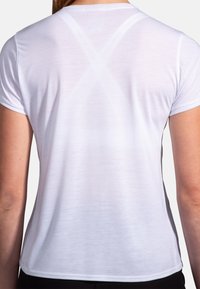 Camisa atlética de manga corta blanca con una textura suave, con un diseño sutil en la parte posterior que muestra costuras cruzadas y lados ajustados.