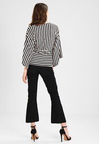 Raidallinen mustavalkoinen paita leveillä hihoilla ja vyötärönauhallisella vyöllä, yhdistetty mustiin leveälahkeisiin housuihin ja korkeakorkoisiin sandaaleihin.