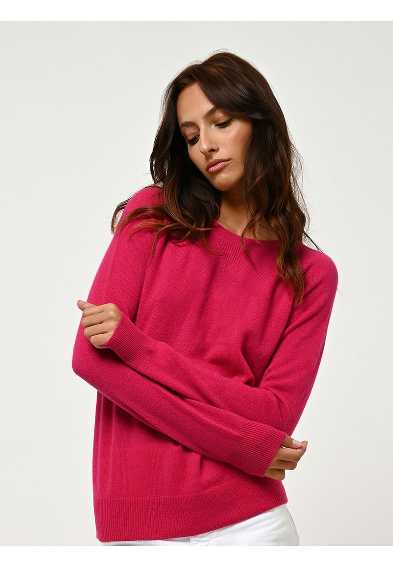 Maglione fucsia lavorato a maglia con maniche lunghe e vestibilità rilassata. Presenta polsini e bordo a coste, scollatura a V e una texture morbida.