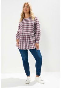 Camicia a maniche lunghe a quadri viola e rosa con vita arricciata, abbinata a jeans aderenti blu e sneakers bianche. Tessuto morbido, vestibilità comoda.