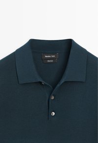 Polo en maille bleu sarcelle foncé avec deux boutons et un col, doté d'une étiquette Massimo Dutti et d'un label indiquant un tissu 100 % coton.