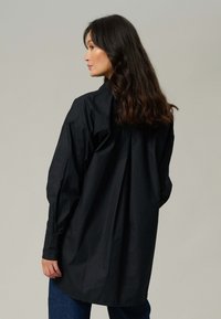 Sort oversized skjorte lavet af bomuld, med lange ærmer, afslappet pasform, knaplukning og en plisseret ryg for ekstra detalje.