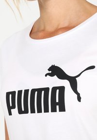 Biała koszulka z wyraźnym czarnym logo „PUMA” i sylwetką skaczącego czarnego kota, wykonana z miękkiej bawełny.