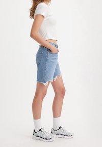Shorts de denim azul claro con bajo deshilachado, cintura alta y cinco bolsillos. Combinados con una camiseta corta blanca y zapatillas deportivas gris-negro.