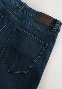 Dunkelblaue Jeans aus Denim mit einem Lederpatch, versehen mit zwei Gesäßtaschen und kontrastierenden Nähten entlang der Nähte. Glatte Textur.