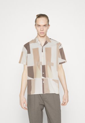 Camisa de manga corta, abotonada en beige claro, con patrones geométricos irregulares en marrón y crema. Tejido suave, corte relajado.