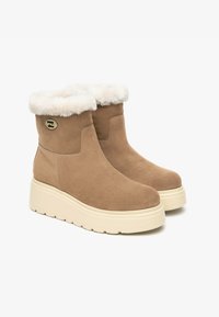 Bottines en daim beige avec un col en fourrure blanche confortable, dotées d'une épaisse semelle en platform crème et d'un accent logo doré sur le côté.
