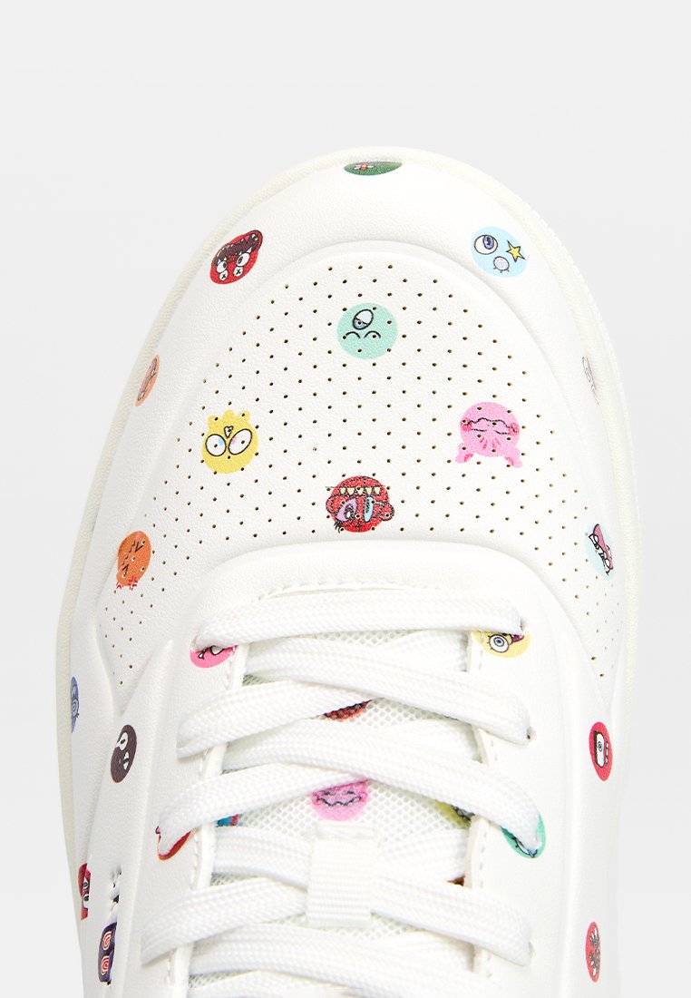 Sneaker blanche avec des motifs de dessins animés multicolores. Présente une texture perforée et des lacets plats. Bout arrondi et semelle rembourrée.