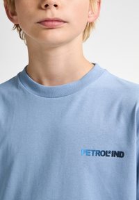 Světle modré bavlněné tričko s kulatým výstřihem, na levé straně hrudi s malým vyšitým logem "PETROLIND" v černé a modré barvě.
