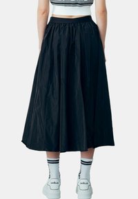 Gonna nera midi con vita arricciata, realizzata in materiale leggero. Indossata con sneakers bianche e calzini a righe. Texture liscia.
