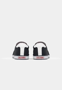 Paire de baskets basses noir et blanc vues de dos avec une étiquette "Hilfiger" rouge et blanche de marque sur les semelles blanches.