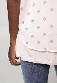 Top rosa claro con lunares a rayas horizontales, tejido suave, dobladillo asimétrico y escote redondeado, combinado con jeans azules.