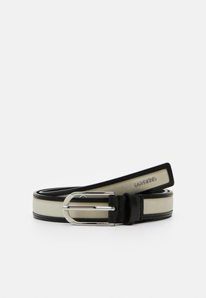 Ceinture en tissu beige avec bords en cuir noir et boucle argentée, ornée du logo "Calvin Klein" sur la ceinture et la boucle.