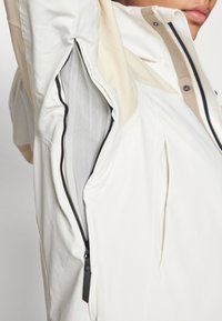 Lightweight white jacket featuring a contrasting beige accent, mesh lining, and black zipper detail on the side pocket.