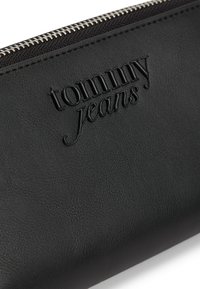 Μαύρο δερμάτινο πορτοφόλι με υφή, με ανάγλυφο λογότυπο "tommy jeans" και ασημένια φερμουάρ.