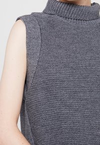 Top senza maniche grigio lavorato a maglia con collo alto, caratterizzato da una finitura testurizzata e una spalla senza cuciture.