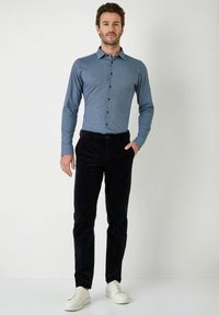 Blauw patroond blouse, donkere corduroy broek en witte sneakers. Slanke pasvorm met een gladde textuur en contrasterende knopen.