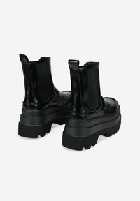 Bottines noires avec une finition en cuir brillant, des panneaux latéraux élastiques, une semelle épaisse et des tirettes à l'arrière pour un enfilage facile.