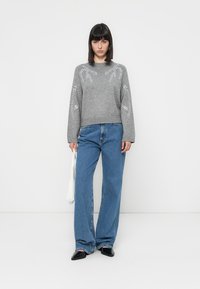Grå strikkegenser med bladbroderi på ermene, kombinert med høyt liv blå denim vide bukser og svarte spisse leiligheter.