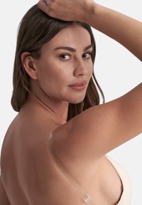 Nude klisterbehå med genomskinliga axelband designad för bruk med rygglös klädsel. Slät textur, osynliga kanter och minimalistisk design för diskret stöd.