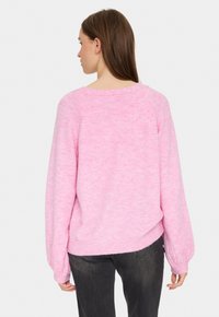 Rosa stickad tröja med en mjuk textur, lös passform och ballongärmar. Har en vid halsringning och ribbat nederkant. Bärs med mörka jeans.