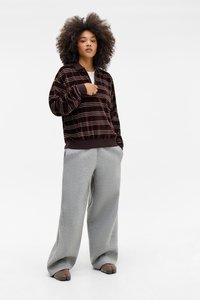 Pullover in velluto a righe marroni con colletto, abbinato a pantaloni della tuta grigi larghi. L'outfit ha una vestibilità comoda e dettagli minimalisti.