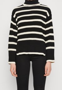 Pull à col roulé rayé noir et crème avec une coupe ample, une texture côtelée et des manches longues. Rehaussé d'un col et d'un ourlet contrastants.