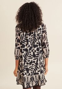 Schwarz-weiß gemustertes Kleid mit Dreiviertelärmeln, weichem Stoff, Rüschen auf der Rückseite und gewelltem Saum.