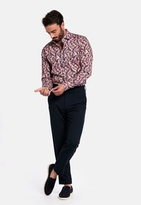 Langarmshirt in roze, blauw en zwart bladdessin; gecombineerd met zwarte broek en zwarte instapschoenen. Soepele stoftextuur.