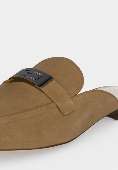 Mule en daim couleur noisette, à enfiler, avec un petit talon et une boucle décorative en métal noir sur le dessus.