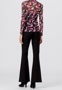 Maglietta a maniche lunghe, trasparente, con audaci motivi geometrici nei colori rosa, grigio e nero; abbinata a pantaloni neri a palazzo e tacchi neri eleganti.